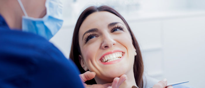 Young woman smiles as a dentist examines her teeth during dental cleaning