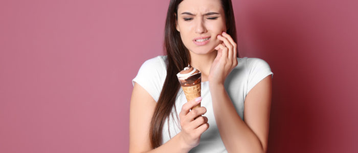 Woman holding ice cream cone wincing in pain from cavity