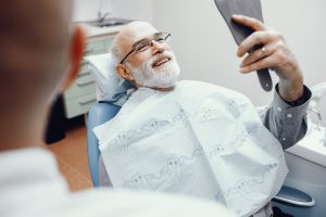 Man smiling and looking at his smile in a dentist chair
