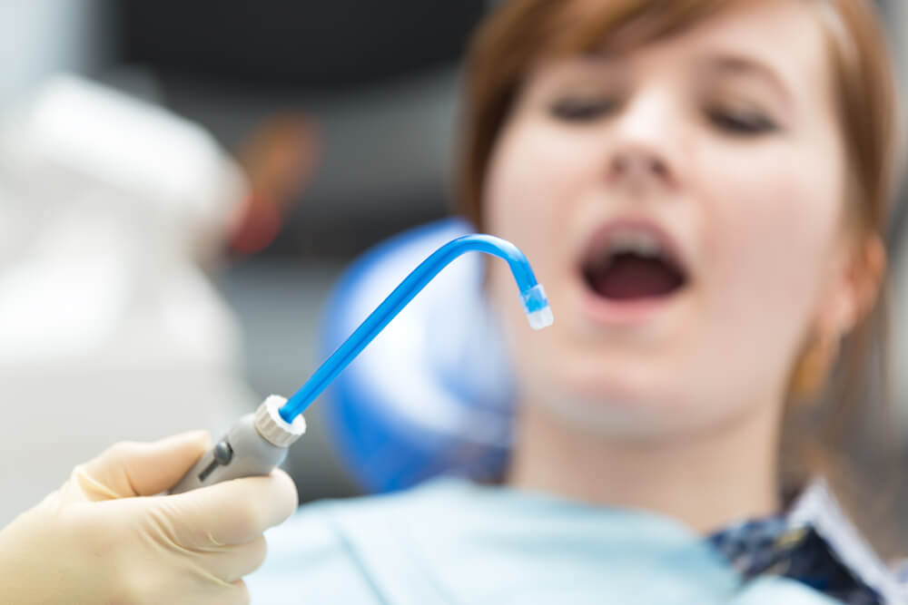 dentist hold a saliva ejector in front of patient's mouth