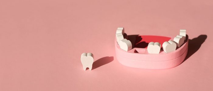 wooden model of a missing tooth on pink background